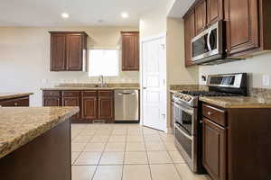Kitchen featuring stainless steel appliances, dark wood finish cabinets, light tile patterned floors, light stone countertops, and recessed lighting