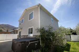 Back of property featuring a mountain view, stone siding, a hot tub, a gate, and a patio area