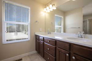 Full bath featuring double vanity, light tile patterned floors, and a shower stall