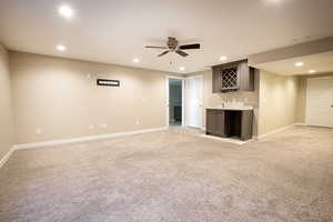 Unfurnished living room with bar with sink, recessed lighting, light carpet, and a ceiling fan