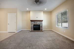 Unfurnished living room with light carpet, a stone fireplace, ceiling fan, light tile patterned flooring, and recessed lighting