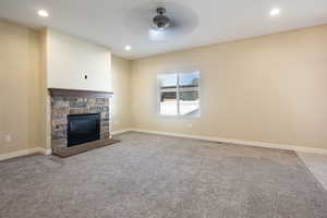 Unfurnished living room with a stone fireplace, a ceiling fan, recessed lighting, and light colored carpet