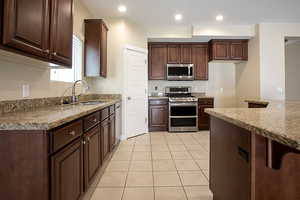 Kitchen featuring stainless steel appliances, light stone counters, light tile patterned flooring, recessed lighting, and a kitchen bar