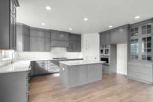 Kitchen featuring gray cabinetry, a kitchen island, light wood-type flooring, light stone counters, and stainless steel double oven