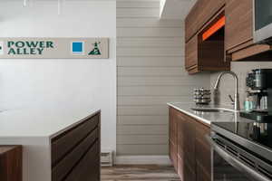 Kitchen with modern cabinets, dark wood finish cabinetry, wooden walls, stainless steel appliances, and baseboard heating