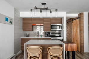 Kitchen with a barn door, stainless steel appliances, tasteful backsplash, modern cabinets, and a breakfast bar area