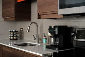 Kitchen with stainless steel microwave, black stove, modern cabinets, backsplash, and dark wood finish cabinetry