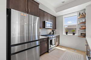 Kitchen with stainless steel appliances, dark wood finish cabinets, backsplash, light wood-style flooring, and open shelves