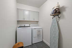 Laundry room with dark tile patterned floors, cabinet space, and independent washer and dryer