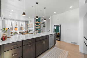 Kitchen featuring a glass covered fireplace, dark wood finish cabinets, light wood-style floors, open floor plan, and stainless steel dishwasher