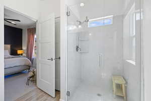 Ensuite bathroom with a marble finish shower, light wood finished floors, and ceiling fan