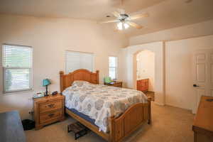 Carpeted bedroom featuring ensuite bathroom, a ceiling fan, arched walkways, and lofted ceiling
