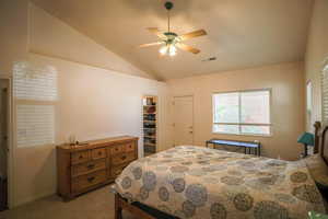 Bedroom with lofted ceiling, a walk in closet, a ceiling fan, and light carpet