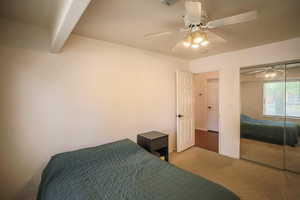 Carpeted bedroom with a closet, a ceiling fan, and beam ceiling