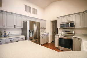 Kitchen featuring stainless steel appliances, dark wood-style flooring, gray cabinets, and lofted ceiling
