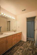 Bathroom with double vanity, dark wood-style flooring, and a shower with curtain