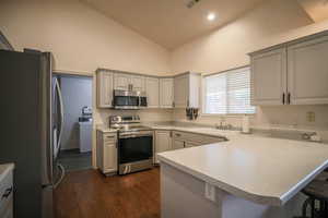 Kitchen with stainless steel appliances, a peninsula, light countertops, lofted ceiling, and dark wood-style flooring