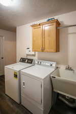 Laundry room featuring a textured ceiling, washer and dryer, dark wood finished floors, and cabinet space