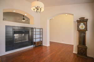 Unfurnished living room featuring a fireplace, arched walkways, dark wood-style flooring, ceiling fan, and a chandelier
