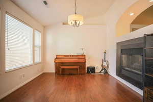 Living area featuring vaulted ceiling, dark wood-style floors, a tiled fireplace, and suspended lighting