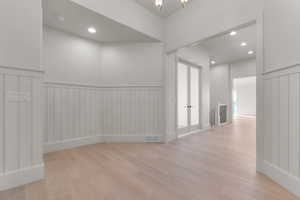 Corridor with a wainscoted wall, light wood-style flooring, and a chandelier