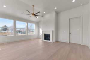 Unfurnished living room with a ceiling fan, lofted ceiling, light wood-style flooring, a glass covered fireplace, and recessed lighting