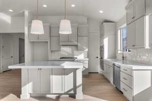 Kitchen with light wood-style floors, vaulted ceiling, a kitchen island, decorative light fixtures, and stainless steel appliances