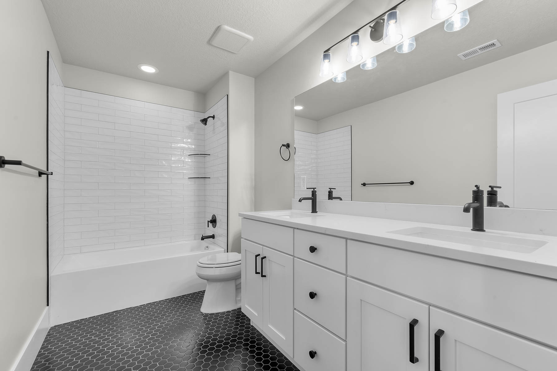 Bathroom featuring double vanity, dark tile patterned flooring, and shower / washtub combination