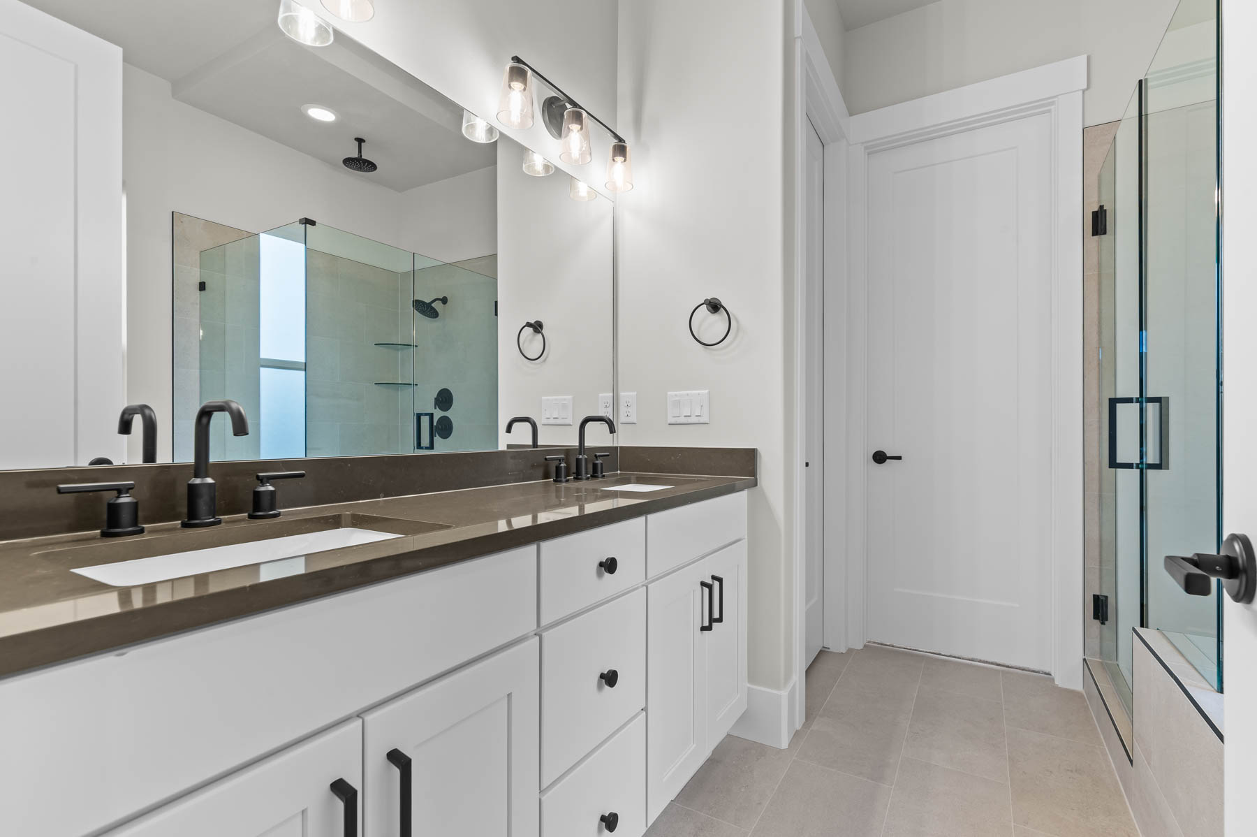 Bathroom with a shower stall, double vanity, and light tile patterned flooring
