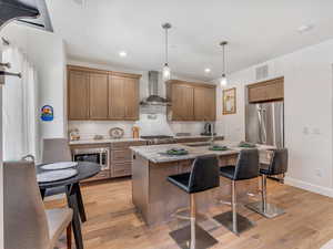 Kitchen featuring light stone countertops, a center island with sink, a breakfast bar, stainless steel appliances, and decorative light fixtures