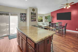 Kitchen featuring a center island, a kitchen breakfast bar, light wood finished floors, a ceiling fan, and light stone counters
