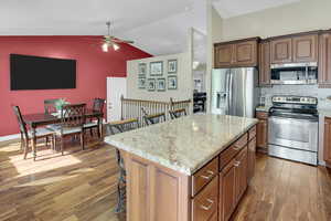 Kitchen featuring stainless steel appliances, a kitchen breakfast bar, vaulted ceiling, decorative backsplash, and dark wood-style floors