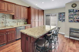 Kitchen with heating unit, backsplash, a breakfast bar area, light stone countertops, and stainless steel dishwasher