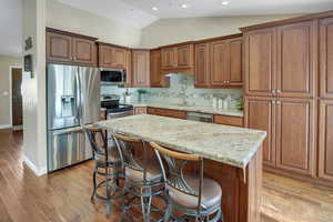 Kitchen featuring stainless steel appliances, decorative backsplash, vaulted ceiling, a breakfast bar area, and light wood finished floors