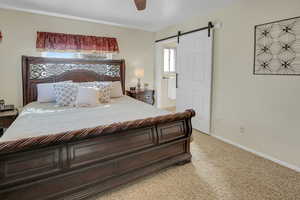 Bedroom featuring a barn door, light colored carpet, and a ceiling fan