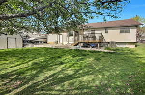 Rear view of house featuring a wooden deck, a yard, a patio, and an outdoor structure