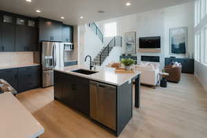 Kitchen with glass insert cabinets, stainless steel appliances, a kitchen island with sink, open floor plan, and dark cabinetry