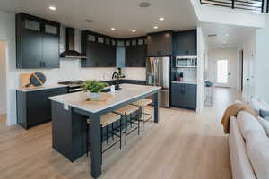 Kitchen with a breakfast bar area, stainless steel appliances, a kitchen island with sink, light wood finished floors, and glass insert cabinets