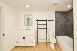 Bathroom with vanity, light wood-type flooring, a textured ceiling, recessed lighting, and bathing tub / shower combination