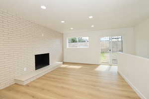Unfurnished living room with brick wall, light wood-style flooring, a fireplace, and recessed lighting
