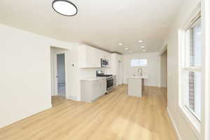 Kitchen featuring stainless steel appliances, a center island with sink, light wood-style flooring, white cabinetry, and recessed lighting