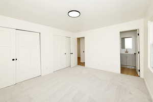 Unfurnished bedroom with two closets, light carpet, and ensuite bath