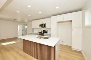 Kitchen with white cabinets, light wood finished floors, stainless steel appliances, an island with sink, and recessed lighting