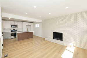 Dual tone kitchen featuring brick wall, open floor plan, stainless steel appliances, a center island with sink, and light countertops