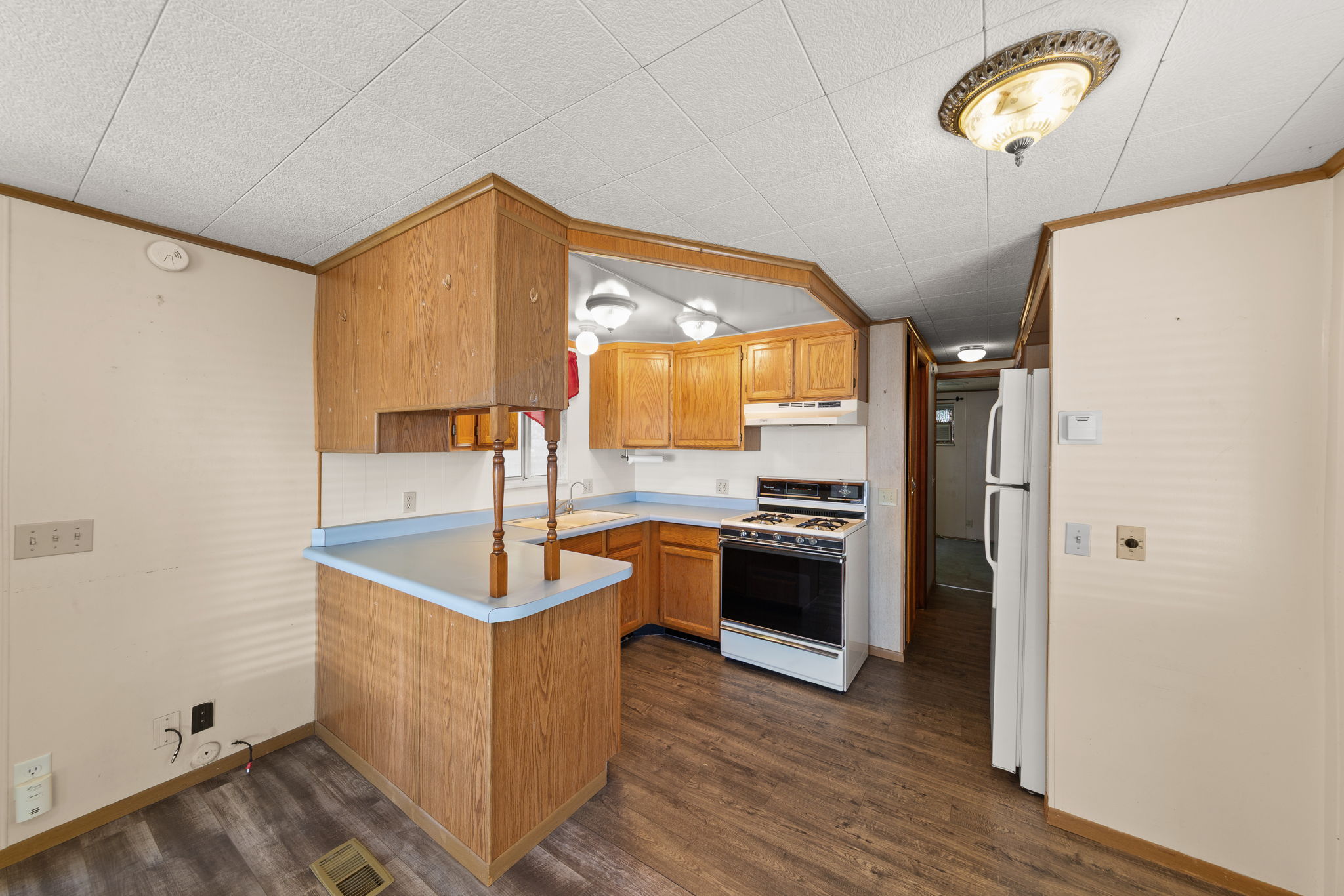 Kitchen with crown molding, a peninsula, light countertops, white appliances, and dark wood finished floors