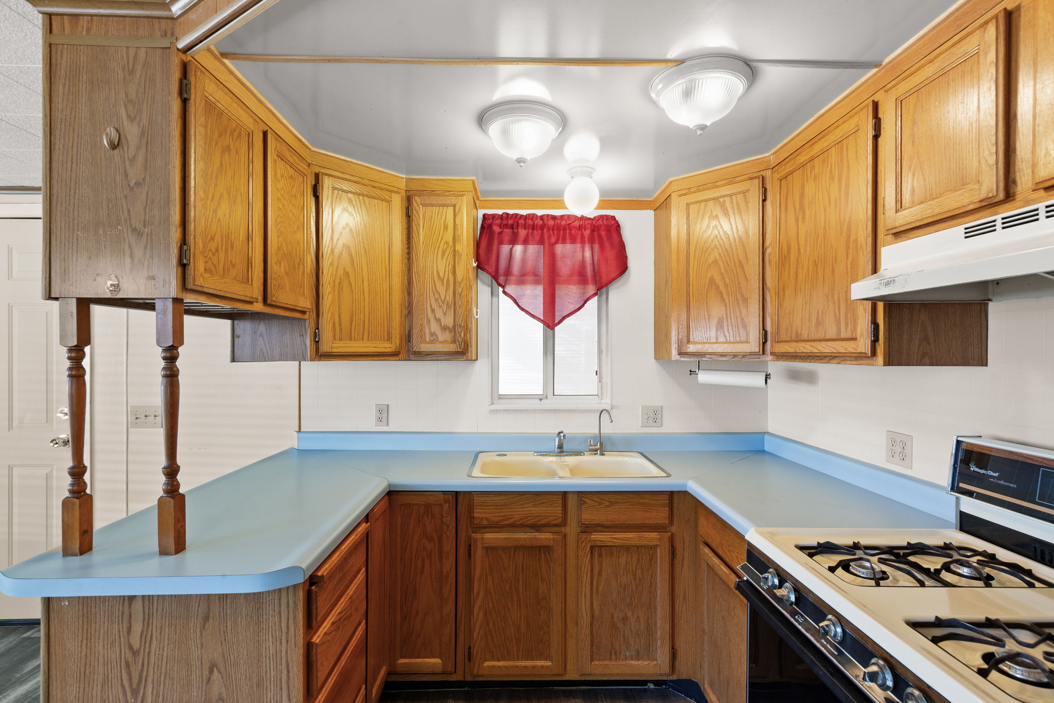 Kitchen featuring gas range, light countertops, wood finish cabinetry, and a peninsula