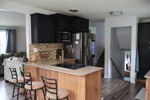 Kitchen with a peninsula, dark cabinets, dark wood-style flooring, and decorative backsplash