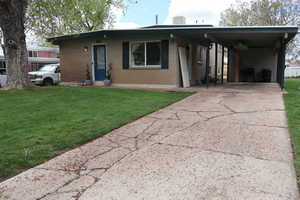 View of front facade with a front yard, concrete driveway, an attached carport, and brick siding