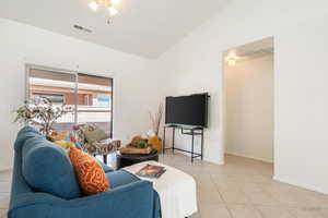 Living room featuring vaulted ceiling, light tile patterned floors, and a ceiling fan