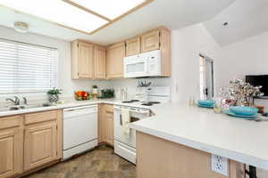Kitchen with light wood finish cabinetry, white appliances, and stone finish floors